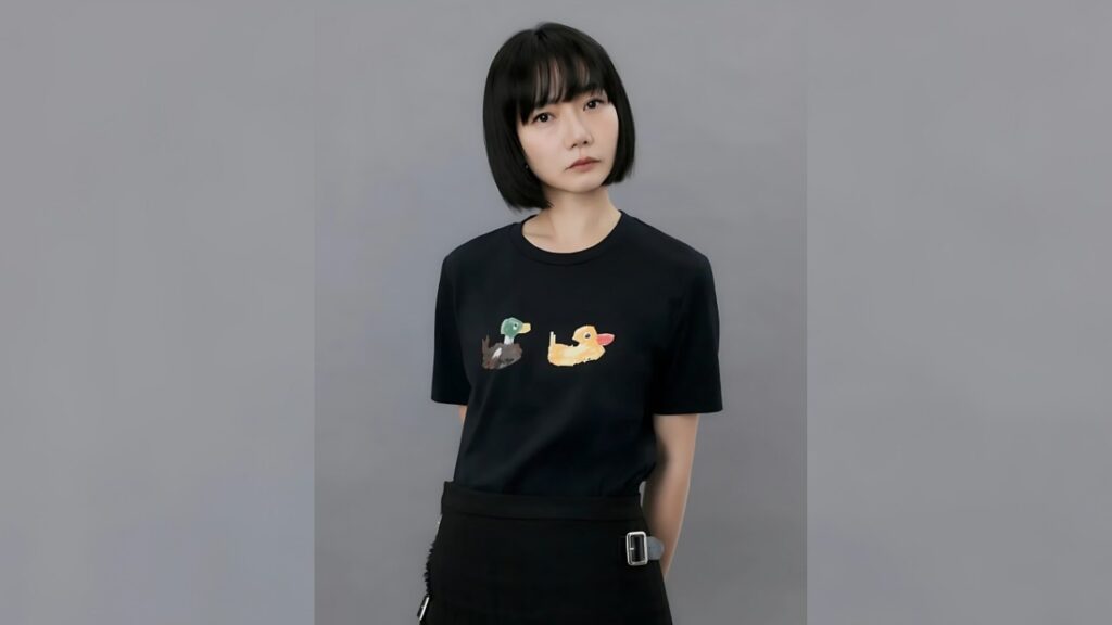 Bae Doona with a short black bob stands against a gray backdrop, wearing a black tee with two small duck graphics.