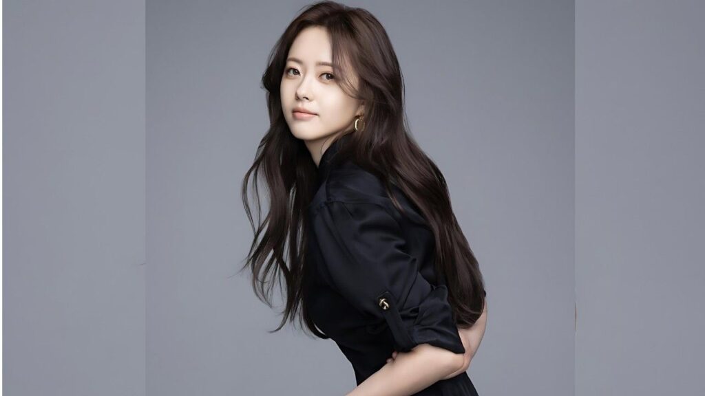 Go Ara with long dark hair in a black blouse leans forward slightly against a gray studio backdrop, soft smile.