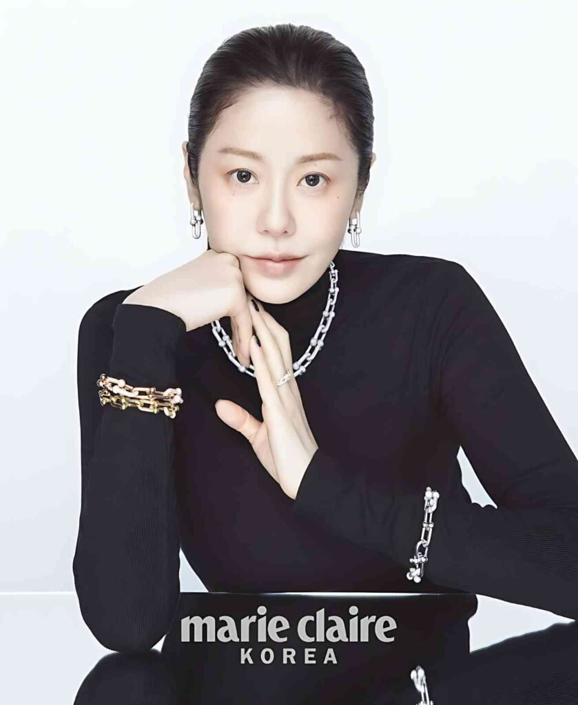 Go Hyun-jung rests her chin on her hands, wearing a black turtleneck and a chunky silver chain necklace with silver earrings.
