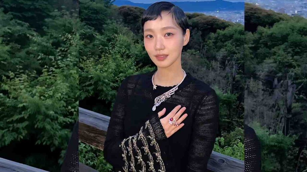 Kim Go-eun with short black hair in a black knit dress, silver beaded fringe, necklace and rings, hand on chest, forest backdrop.