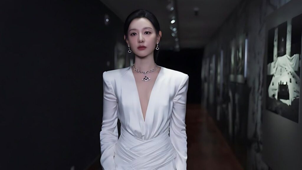 Kim Ji-won in a white draped gown with a deep V-neck stands in a dim gallery hallway, wearing necklace and earrings.