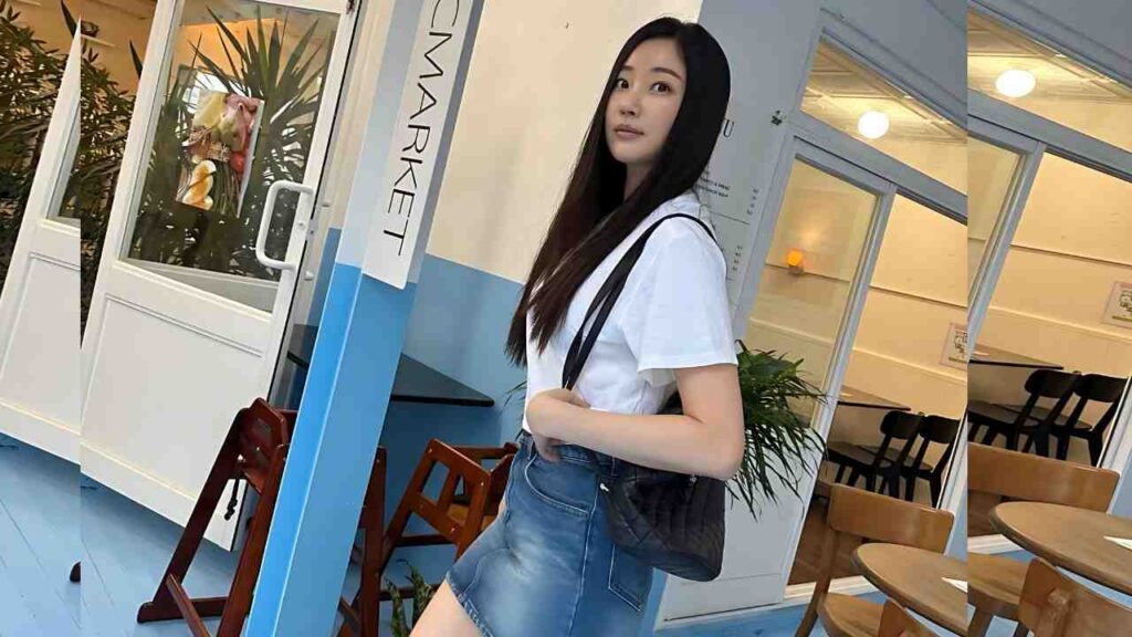 Kim Sa-rang with long dark hair in a white tee and denim skirt, carrying a black quilted bag, posing by a blue cafe.