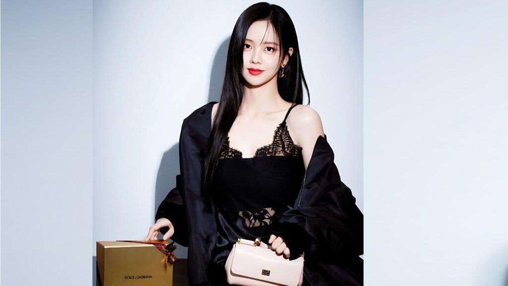 Kim So-hyun Long black hair, black lace top with satin jacket, holding a pale pink handbag beside a gold gift box on a pale blue wall.