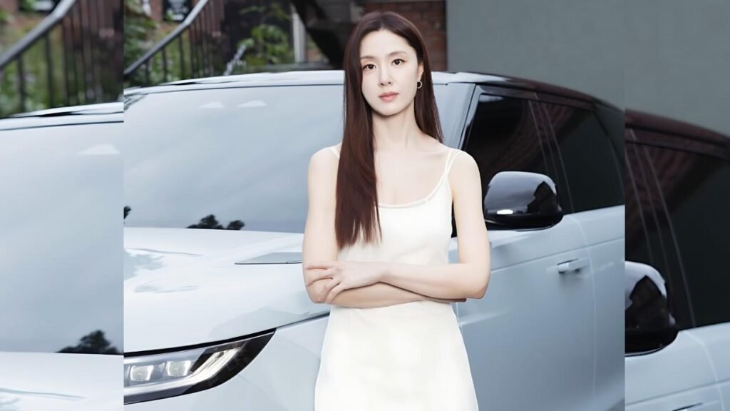 Seo Ji-hye ( 서지혜 ) with long dark hair stands with arms crossed beside a gleaming white SUV, wearing a pale satin tank dress.