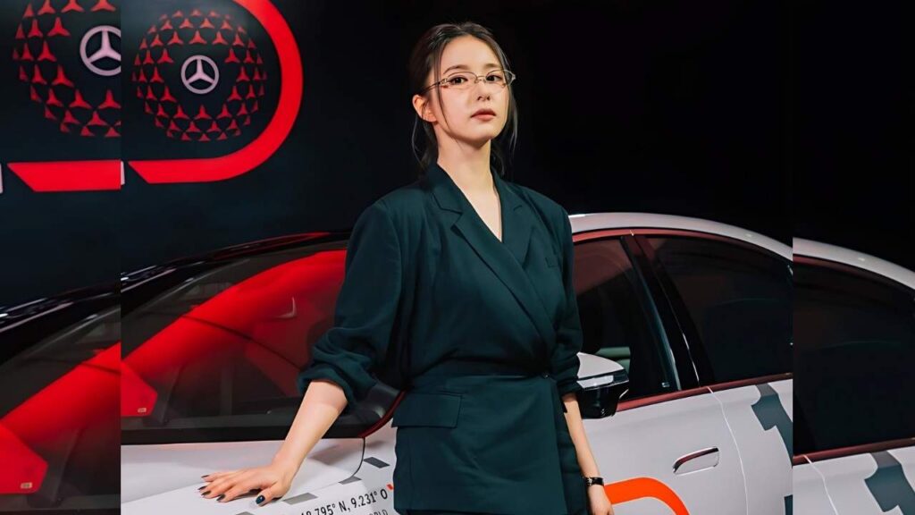 Shin Se-kyung in a dark teal blazer leans against a white car at an auto show, with red Mercedes logos on a black backdrop.