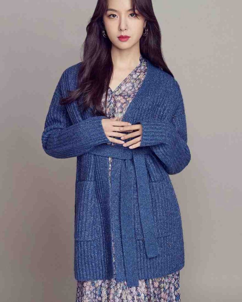 seo ji-hye boyfriend with long dark hair, wearing a blue knit cardigan over a floral dress, hands folded at her waist.