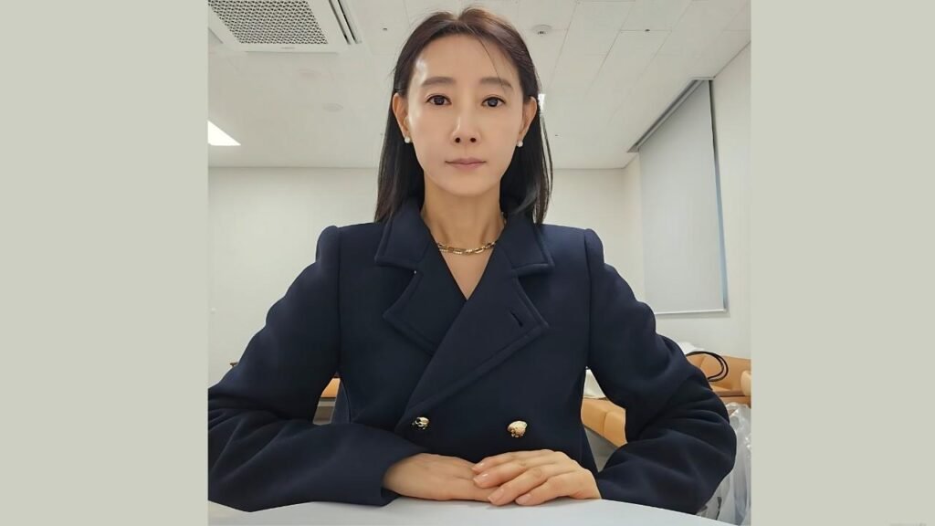Do Ji-won (도지원) in a navy double-breasted blazer with gold buttons, seated with hands clasped in an office.