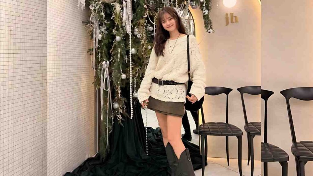 Go Bo-gyeol in a white knit sweater and olive mini skirt poses beside a decorated Christmas tree with a black crossbody bag.