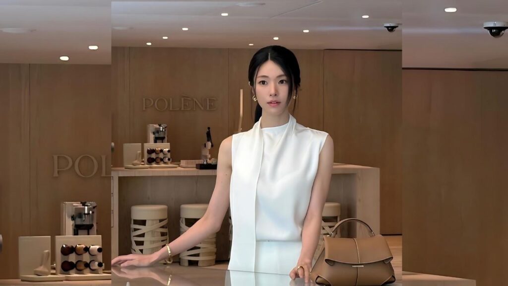 Ha Young in a sleeveless white top stands at a light wood counter in a beige POLENE boutique, with tan handbag nearby.