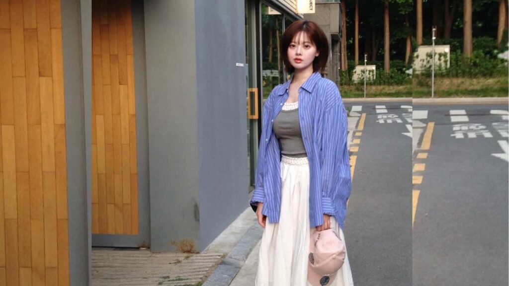 Han Soo-ah on a city sidewalk wearing a blue striped shirt over a gray top, white skirt, and carrying a pink bag.