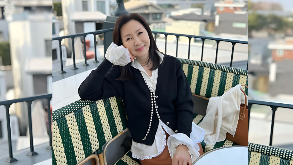 Jeon In-hwa on a green balcony bench, wearing a black cardigan over a white lace blouse with pearls; brown bag beside her.