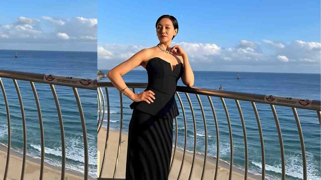 Jin Kyung in a strapless black gown with peplum, wearing a necklace, poses on a seaside balcony with blue ocean behind.