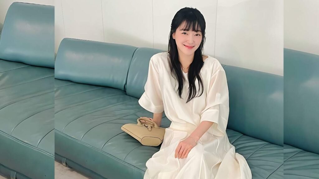 Jo Woo-ri (조우리) with long black hair and bangs sits on a teal couch in a flowing white dress, beige handbag beside her.
