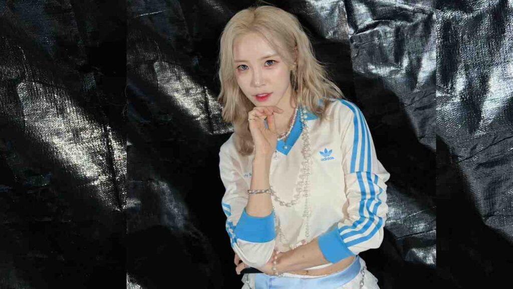 Jun Hyo-seong (전효성) in a white Adidas jacket with blue stripes, pearl necklace, posing with hand on chin against a dark backdrop.