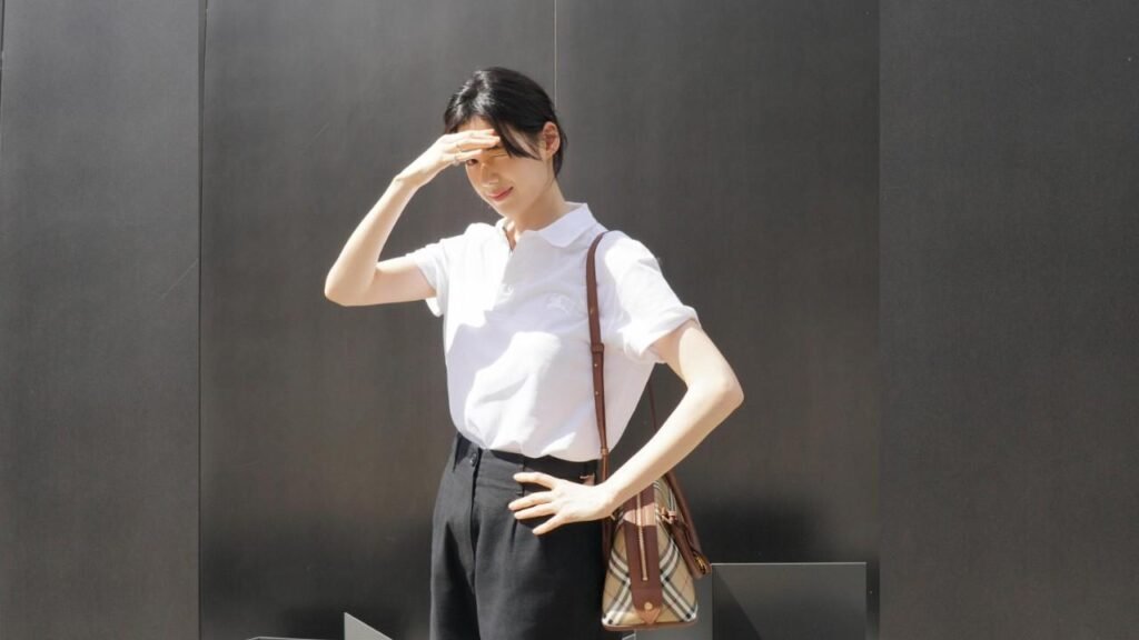 Jung Eun-chae (정은채) shielding her eyes with a raised hand, wearing a white polo and black trousers, with a brown plaid crossbody bag.