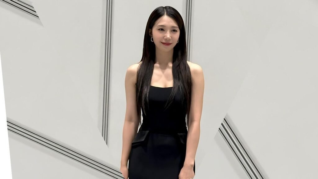Jung Eun-ji with long black hair wearing a black sleeveless dress stands against a white geometric backdrop, soft smile.