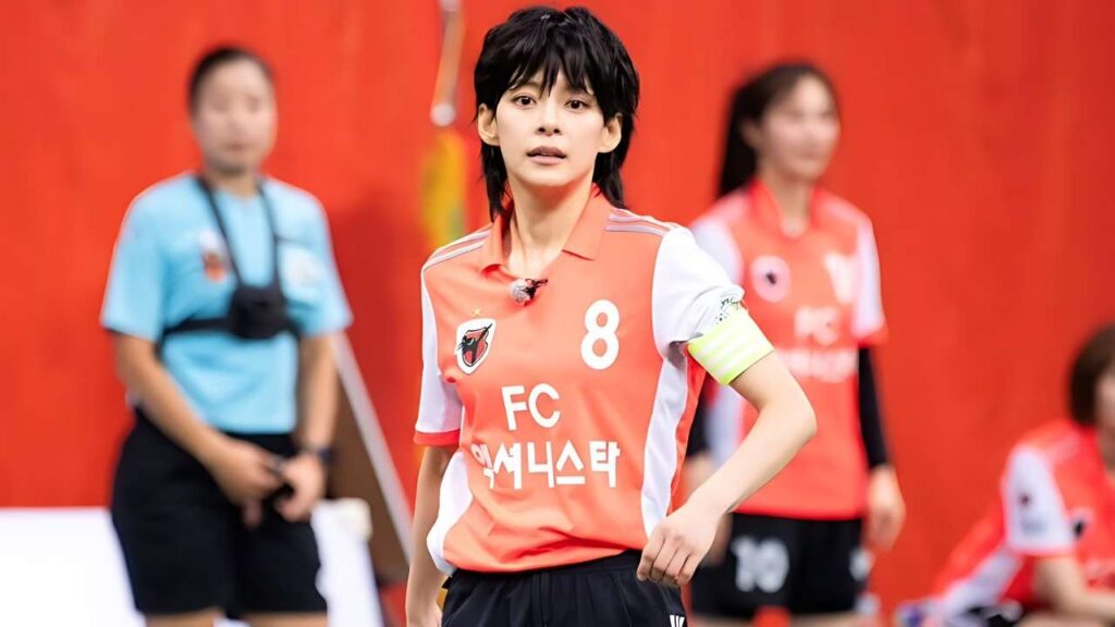 Jung Hye-in (정혜인) in orange jersey with number 8 and yellow armband, standing on a red backdrop with blurred teammates.