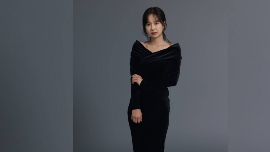 Jung Min-gyul in a black velvet off-shoulder dress stands against a gray studio backdrop, arms crossed with a calm expression.
