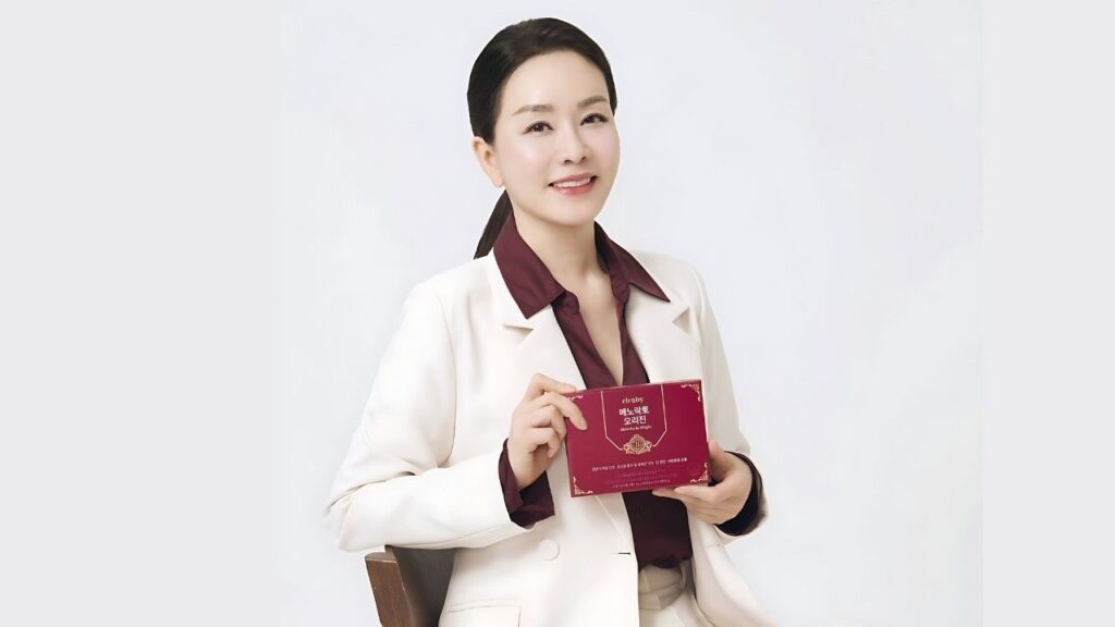 Kim Jung-nan (김정난) in a cream blazer sits against a white background, holding a maroon booklet with a gold emblem.