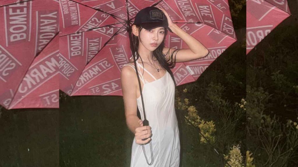 Kim Min-ji (김민지) in a white slip dress and black cap outdoors at night, holding a large pink umbrella with white text.
