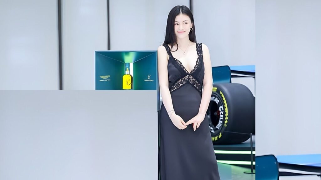 Kim Yong-ji (김용지) in a lace-trimmed gown stands beside a case with a yellow bottle, smiling as a race car tire is visible behind.