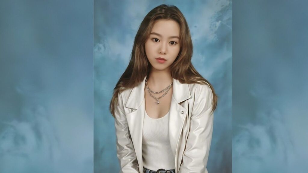 Kwak Ji-min with long light brown hair, wearing a white jacket over a white top, layered necklaces, against a blue backdrop.