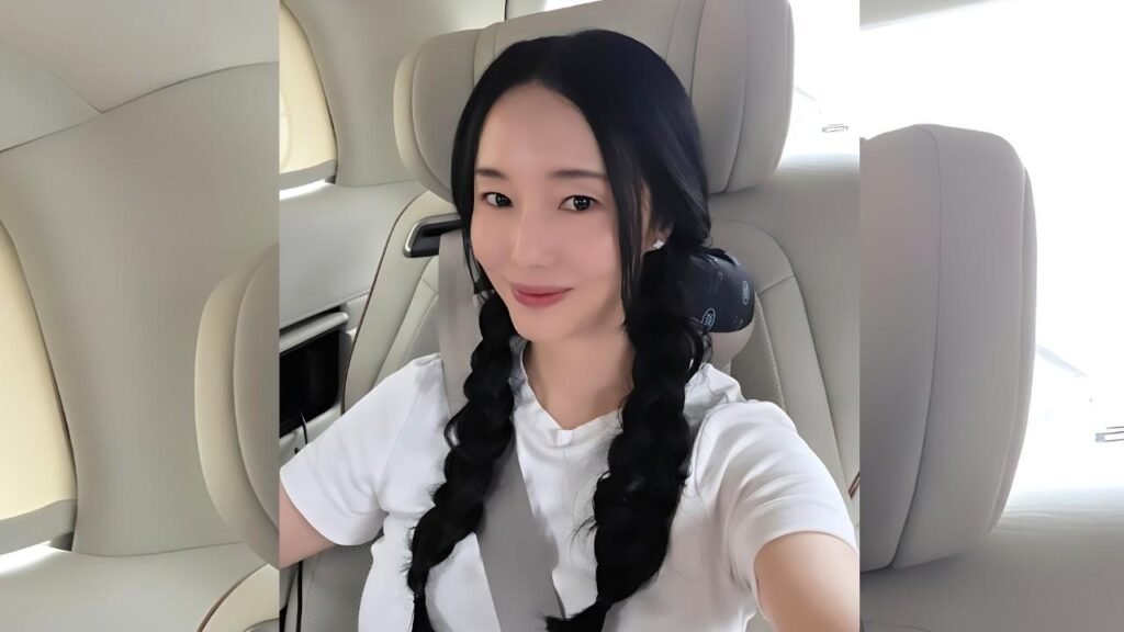 Lee Jung-hyun with two braids wearing a white shirt, seated in a cream car with a seatbelt, smiling while taking a selfie.