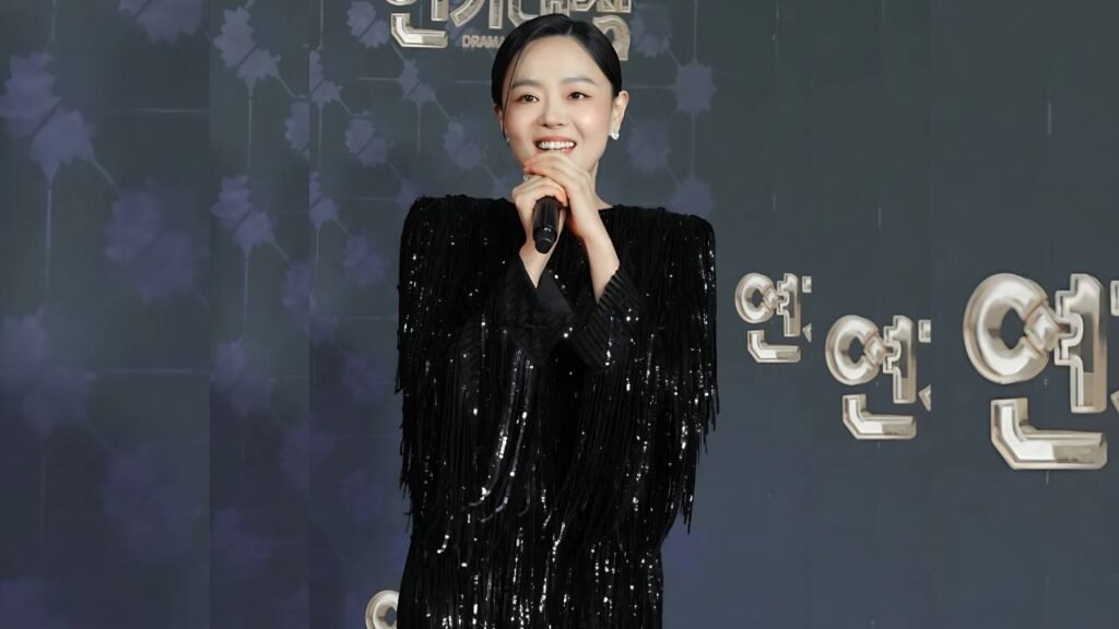 Lee Sang-hee (이상희) in a black sequined fringe dress holds a microphone on stage, against a dark backdrop with metallic letters.