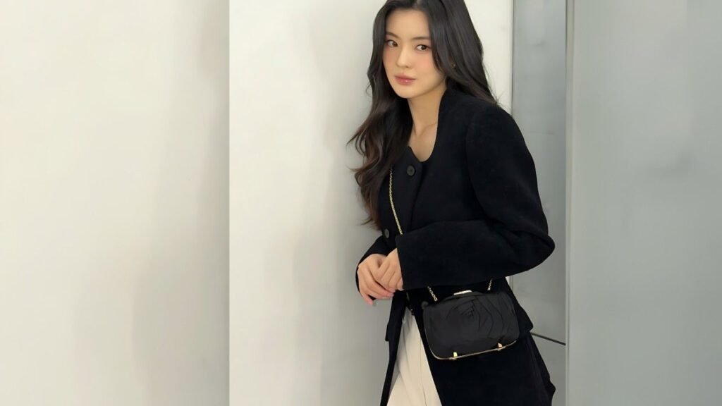 Lee Sun-bin with long dark hair in a black coat and white outfit, carrying a black quilted crossbody bag with a gold chain.