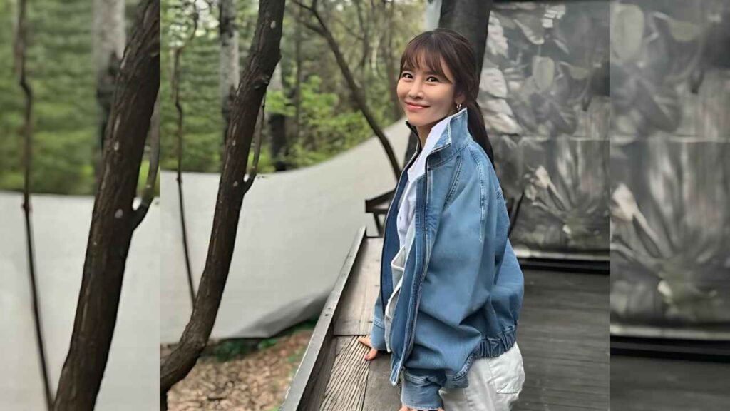Lee Yeon-doo (이연두) in a blue denim jacket and white top with a ponytail leans on a wooden railing, smiling in a tree-lined outdoor space.