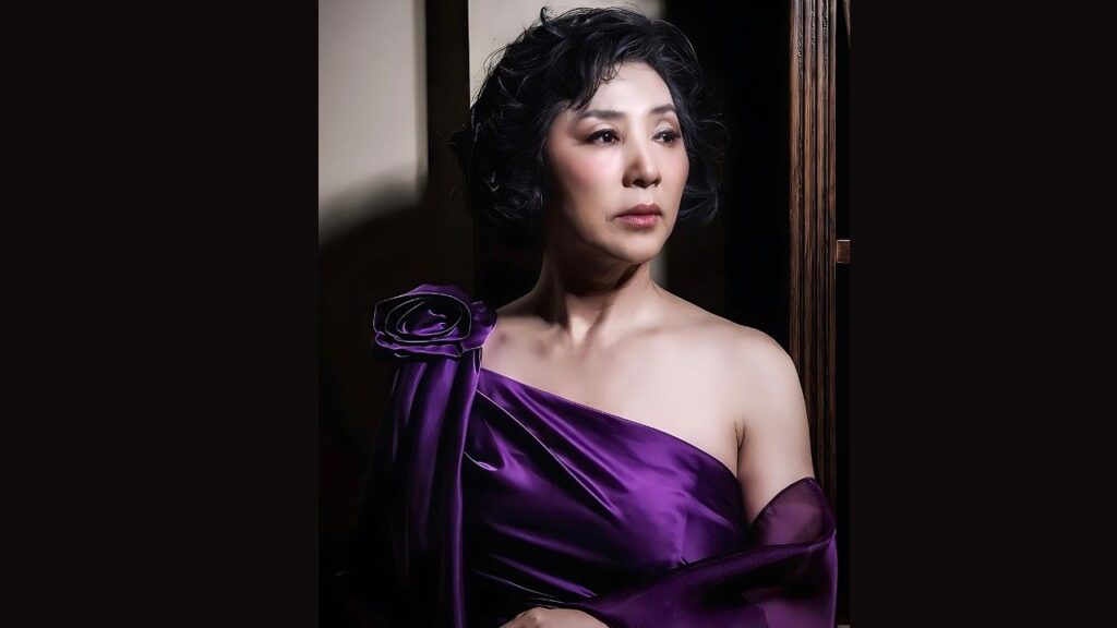 Lim So-young in a satin purple one-shoulder gown with a rose, short curly hair, gazing to the side in a dim wooden doorway.