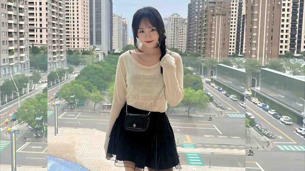 Min Chae-yeon (민채연) with a side braid in a cream sweater and black skirt stands on a glass balcony, overlooking a street with trees.
