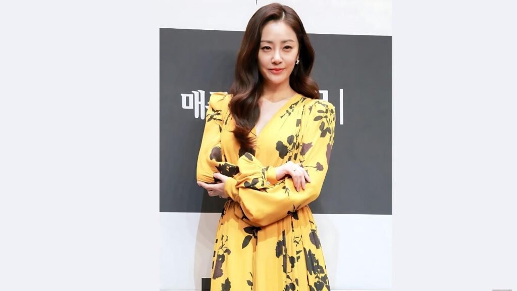 Oh Na-ra in a yellow floral dress with voluminous sleeves stands with crossed arms against a black-and-white backdrop.