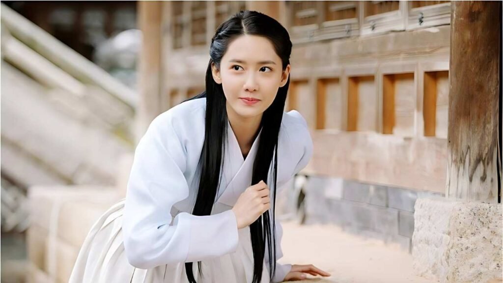 Park Min-ji (박민지) in a white dress with long black hair, leaning by a wooden wall, one hand on a stone ledge, serene smile.