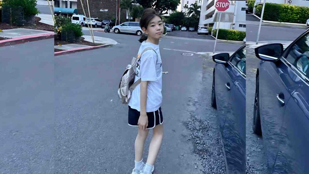 Park So-yi in a light blue tee, black shorts, and a gray backpack stands in a parking lot beside blue car, looking at camera.