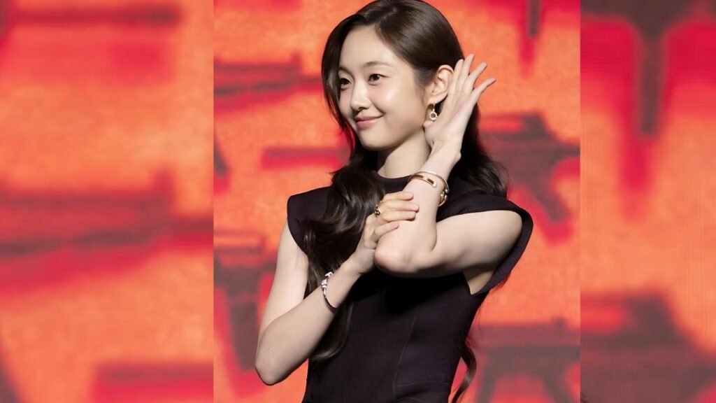 Park You-na with long dark hair in a black sleeveless dress poses before a warm orange-red backdrop, touching her ear.