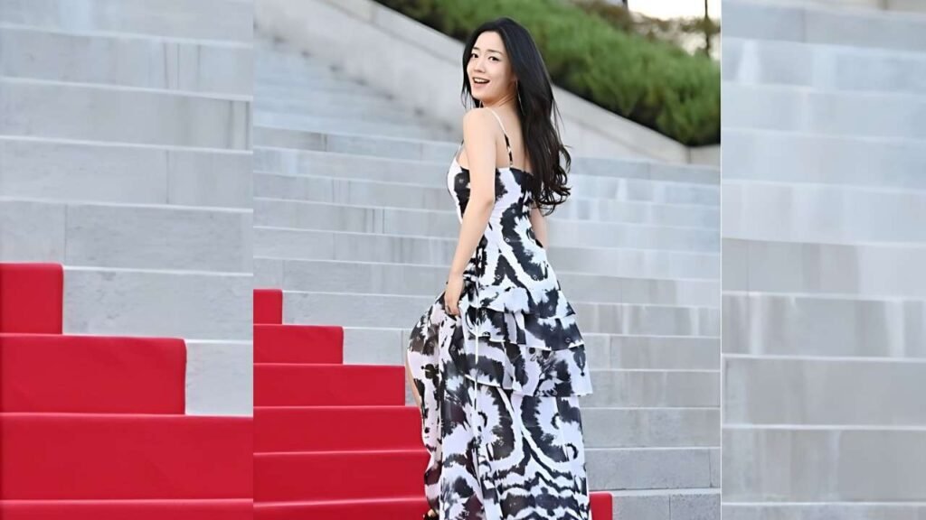 Ryu Hwa-young with long dark hair in a black-and-white tiered dress poses on gray steps beside red seating, looking back.