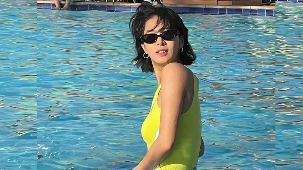 Seo Rina (서리나) in a bright yellow one-piece swimsuit and black sunglasses stands in a blue pool, angled to the side.
