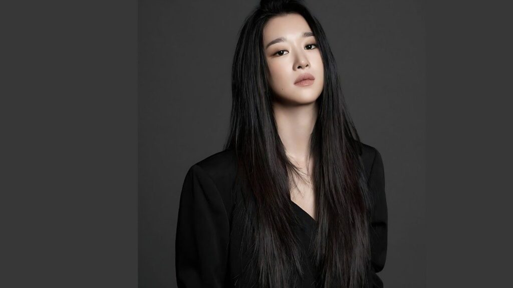 Seo Yoo-jung with long, straight black hair and a black top stands against a dark gray studio backdrop, calm expression.
