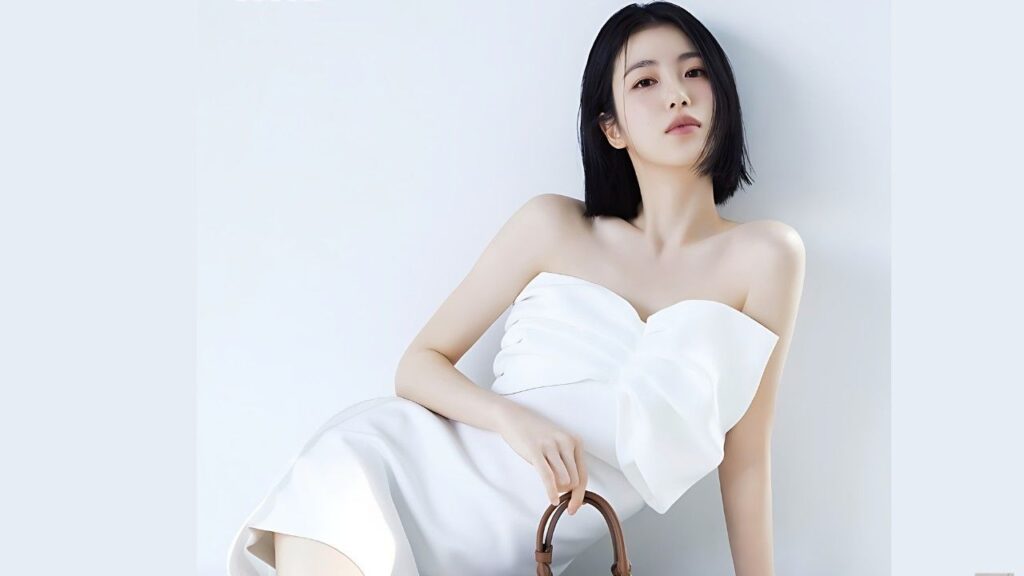 Shin Ye-eun (신예은) in a strapless white dress with a large bow, leaning against a pale blue wall while holding a brown bag handle.