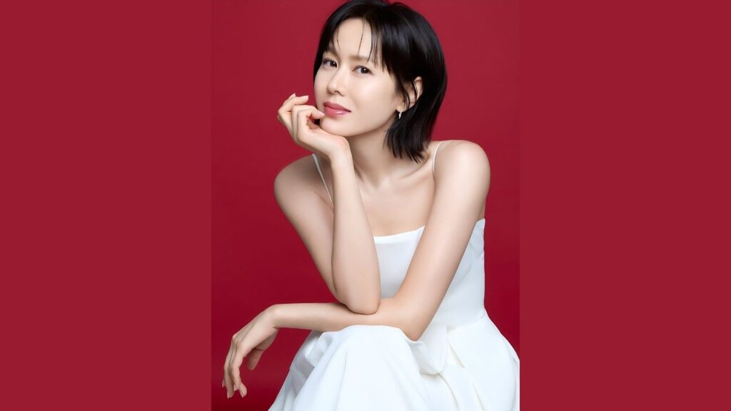 Son Ye-eun (손예은) with short black hair in a white spaghetti-strap dress, chin resting on her hand against a red backdrop.