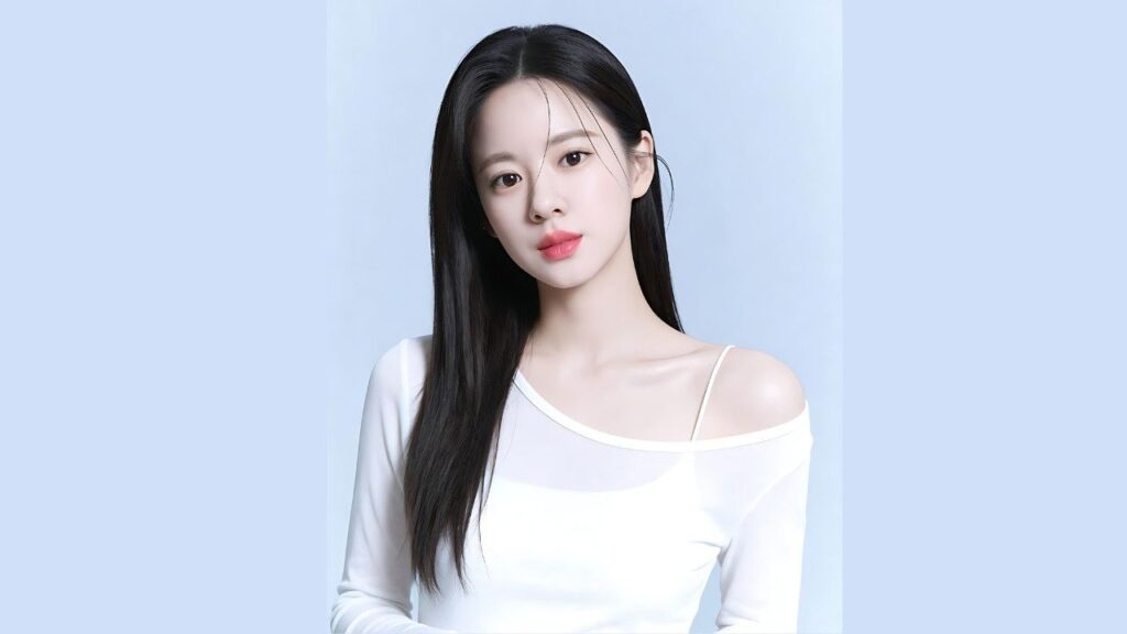 Song Eun-jin with long black hair stands against a pale blue background, wearing a white off-shoulder top with a thin strap and a soft gaze.
