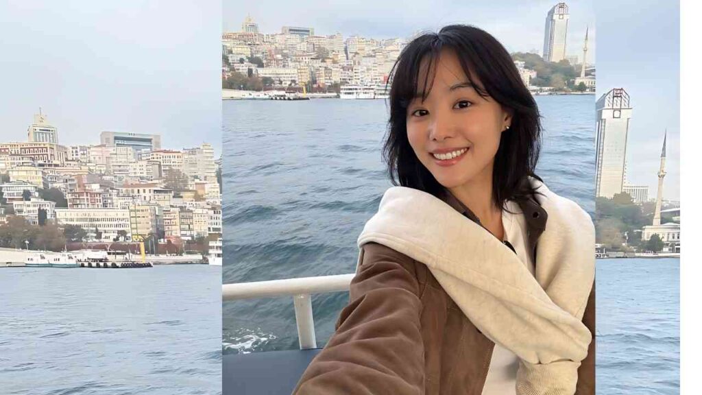 Song Ji-eun (송지은) on a boat selfie, cream scarf, brown jacket, with water and skyline behind.