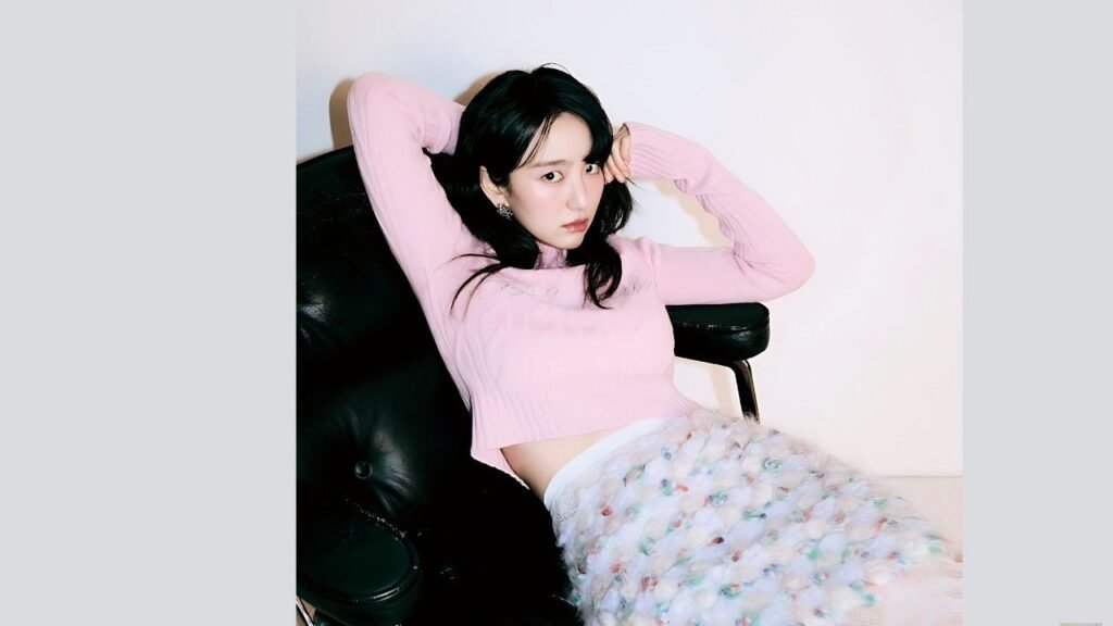 Won Jin-ah reclining in a black leather chair, hands behind her head, wearing a pink cropped sweater and pastel fuzzy skirt, gazing at the camera.