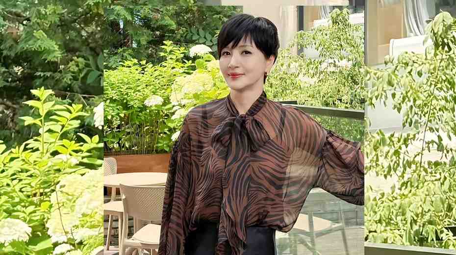 Yoon Hae-young with short black hair in a sheer brown zebra-print blouse stands beside a glass railing amid lush cafe greenery.
